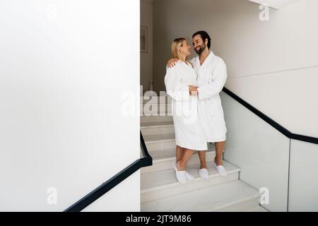Un couple magnifique portant des peignoirs blancs et profitant d'un week-end au spa pendant une lune de miel à pied au centre de bien-être Banque D'Images