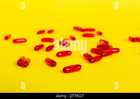 Tas de pilules rouges sur fond coloré. Tablettes dispersées sur une table. Pile de capsule de gélatine molle rouge. Vitamines et compléments alimentaires concept. Banque D'Images