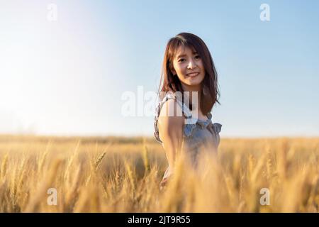 Belle et heureuse femme asiatique profitant de la vie dans le champ d'orge au coucher du soleil. Banque D'Images