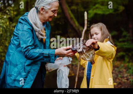 Petite fille avec grand-mère montrant les déchets de plastique ce qu'ils ont trouvé des outoors en forêt. Banque D'Images