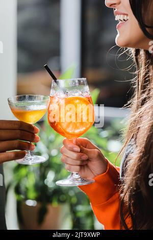 Vue rognée d'une femme gaie en toaster un cocktail avec un ami afro-américain dans un café, image de stock Banque D'Images