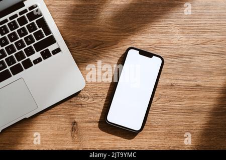 Téléphone mobile avec écran tactile maquette blanc vierge et ordinateur portable sur le bureau, plan de travail avec vue sur le dessus et espace de copie pour les communications professionnelles et Banque D'Images