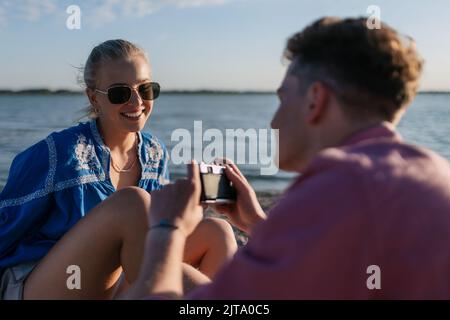 Jeune garçon prenant la photo de sa belle petite amie à la plage pendant le coucher du soleil. Banque D'Images