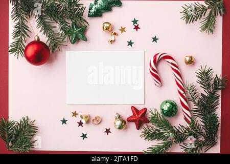 Maquette de carte de Noël. Carte de voeux vide plat avec décorations de noël rouges, branches de sapin et ornements sur fond rose. Carte postale moderne Banque D'Images