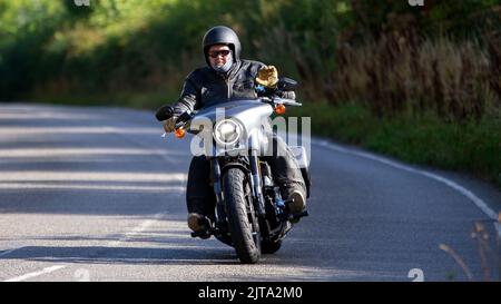 Homme à bord d'une moto Harley Davidson sur une route de campagne anglaise Banque D'Images