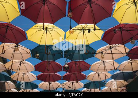 Vue de face détail de parasols colorés et d'ampoules Edison accrochés au-dessus d'une rue de la ville contre un ciel bleu Banque D'Images