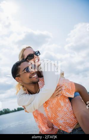 joyeux afro-américain homme coggydorant petite amie tout en regardant loin Banque D'Images