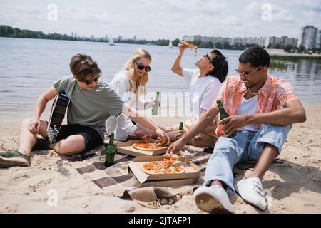 jeunes amis multiethniques mangeant de délicieuses pizzas et buvant de la bière sur la plage Banque D'Images