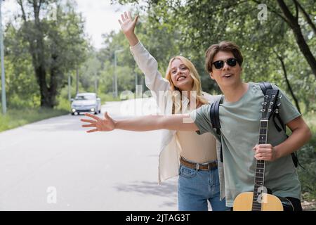 couple souriant se faisant passer les mains et arrêtant la voiture tout en s'accrochant à la campagne Banque D'Images