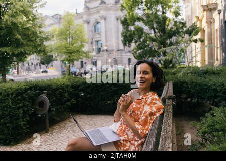 étonnant jeune indépendant dans la tenue d'été assis sur banc avec des dispositifs dans le parc vert à berlin, image de stock Banque D'Images