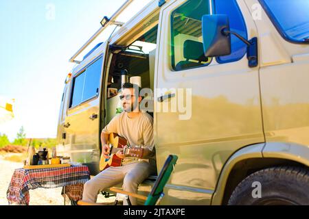 Le jeune homme est assis au seuil du camion-remorque et joue de la guitare Banque D'Images