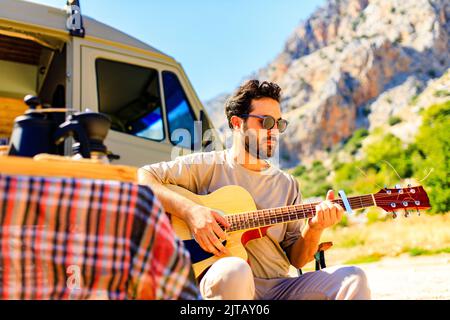 Le jeune homme est assis près d'un camion de remorque et joue de la guitare Banque D'Images