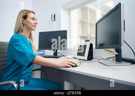 Femme vêtue de vêtements bleus assis à une table et travaille à un ordinateur Banque D'Images