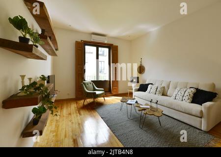 Séjour d'une maison avec grand canapé beige avec coussins, balcon avec volets en bois, étagères en bois brut avec plantes et de la fl en bois d'origine Banque D'Images