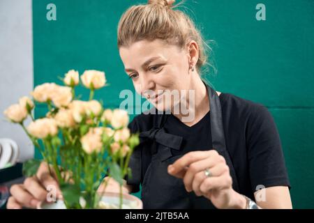 Fleuriste souriant créant un arrangement de fleurs dans la boutique de fleurs Banque D'Images