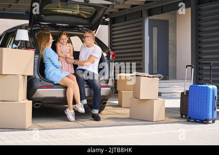 Les parents s'assoient en voiture avec le coffre ouvert et la fille tickle Banque D'Images