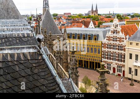 Le Stadhuiskwartier à Deventer, l'une des neuf villes hanséatiques historiques sur la rivière IJssel, dans la province d'Overijssel, aux Pays-Bas, est l'extension de l'hôtel de ville achevée en 2016 par les architectes Neutelings Riedijk. Sa façade en verre encadrée de jaune porte l'œuvre d'art « Deventer Raamwerk » (Cadre de Deventer) de l'artiste Loes ten Anscher : 2 264 empreintes digitales de résidents de Deventer moulées en aluminium. Vu depuis la tour de l'église Saint-Lebuïnus, le bâtiment se dresse à côté d'une maison à pignon en escalier avec une porte rouge, la toiture de la vieille ville et plusieurs clochers d'église étant visibles à l'horizon derrière lui. Banque D'Images