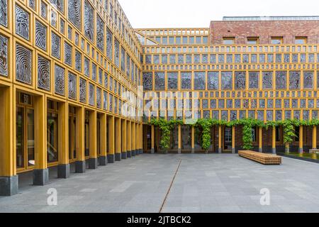 Le Stadhuiskwartier à Deventer, l'une des neuf villes hanséatiques historiques sur la rivière IJssel, province d'Overijssel, Pays-Bas, est l'extension de l'hôtel de ville achevée en 2016 par les architectes Neutelings Riedijk. Sa façade en verre encadrée de jaune porte l'œuvre d'art „Deventer Raamwerk“ (Cadre de Deventer) de l'artiste Loes ten Anscher : 2 264 empreintes digitales de résidents de Deventer moulées en aluminium. Une cour pavée avec un banc en bois et de la verdure grimpante à l'entrée du „Stadhuis“ se trouve dans la cour du bâtiment en forme de L. Banque D'Images