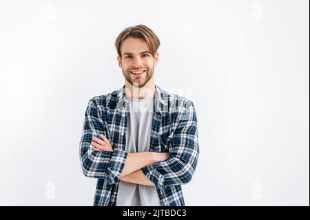 Portrait d'un homme de style caucasien positif et confiant aux yeux bleus, debout sur un fond blanc isolé avec des bras croisés, regardant l'appareil photo, souriant amical Banque D'Images