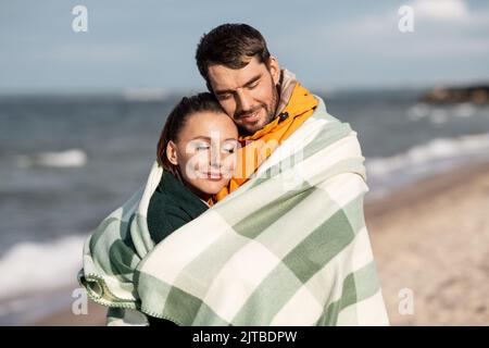 couple heureux dans une couverture chaude sur la plage d'automne Banque D'Images