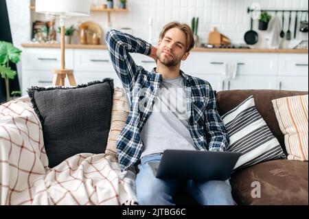 Contrarié caucasien jeune homme élégant, assis sur un canapé dans un salon confortable, massant son cou, fatigué après une dure journée au travail et en ligne, souffrant de problèmes articulaires, nerf pincé dans le cou, besoin de repos Banque D'Images