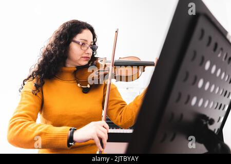 Brunette femme portant un chandail jaune, et jouant du violon en lisant de la musique en feuilles. Banque D'Images