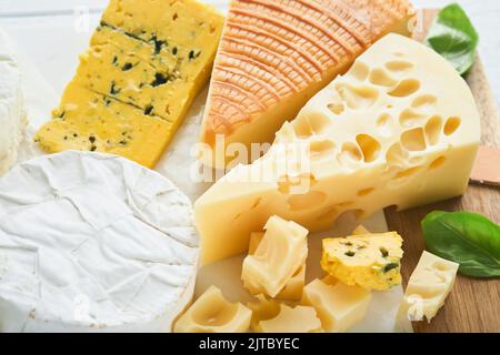 Morceau de maasdam et de camembert, fromage fumé, fromage bleu, parmesan, brie au basilic et poivre sur plateau de marbre blanc vieux bois Banque D'Images