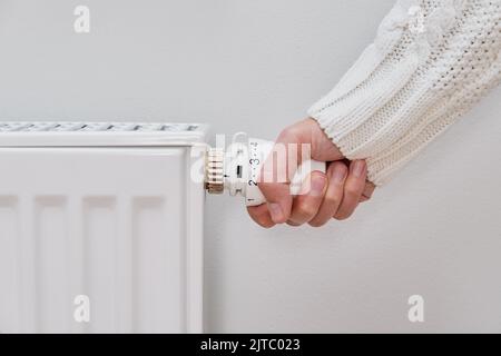 Femme ajustant la température sur le radiateur de chauffage, concept de crise énergétique en Europe, augmentation des coûts dans les ménages privés pour la facture de gaz en raison de l'inflation et de la guerre Banque D'Images