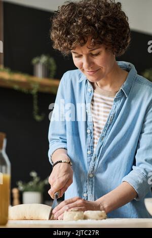 Jeune femme coupant de la pâte maison avec un couteau à table pour cuire des petits pains Banque D'Images