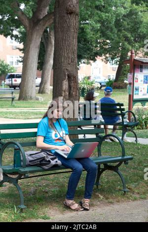 Jeune femme adulte utilisant un ordinateur portable Apple tout en étant assise sur un banc de parc. Banque D'Images