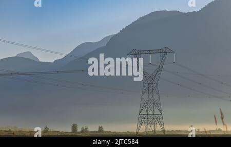 Lignes électriques haute tension au lever du soleil dans le matin brumeux, tour de transmission électrique haute tension. Lignes haute tension passant par un champ labouré Banque D'Images