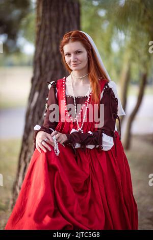 Portrait d'une jolie fille mince à cheveux rouges dans une robe rouge à la mode vénitienne du 15th siècle Banque D'Images