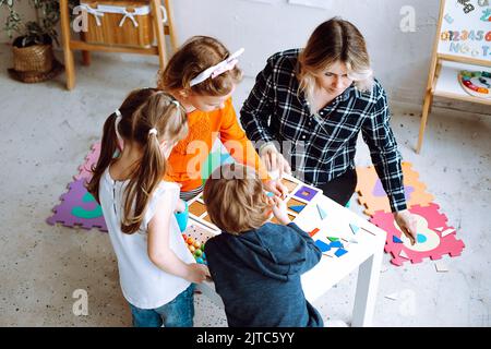 Les enfants qui s'intéressent jouent avec des jouets éducatifs sur le bureau, assis au sol, vue sur le dessus. Un éducateur et des enfants plient le constructeur dans la salle de jeux Banque D'Images