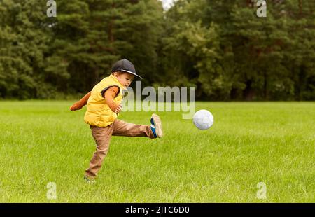 petit garçon avec ballon jouant au football au parc Banque D'Images