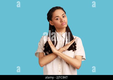 Rien, jamais plus. Portrait d'une femme sérieuse déterminée avec des dreadlocks noirs croisant les mains sur la poitrine, gestante x signe, arrêter c'est la fin. Studio d'intérieur isolé sur fond bleu. Banque D'Images