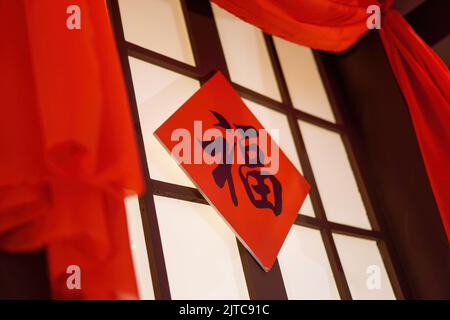 Une photo sous angle de calligraphie chinoise écrite sur une planche carrée suspendue sur une fenêtre fermée avec un tissu rouge entourant la fenêtre Traduction: Chance Banque D'Images