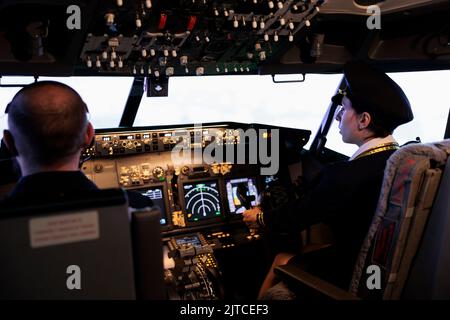Avion de ligne femelle en avion volant uniforme avec boutons de commande de cockpit sur le tableau de bord de la cabine. Appuyer sur l'interrupteur du moteur et du radar sur la carte du panneau de commande pour piloter le jet avec la navigation routière. Banque D'Images