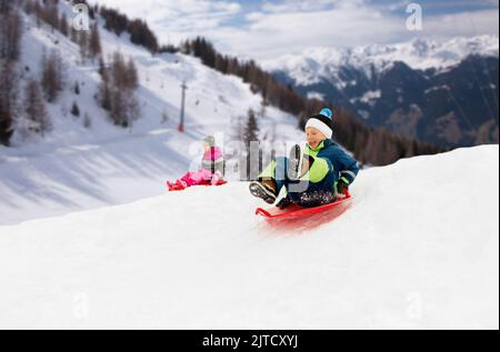 Happy kids sur des traîneaux glissant en bas de la colline en hiver Banque D'Images