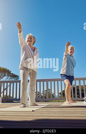 Améliorer la santé dans les années d'or. Un couple senior faisant du yoga ensemble sur leur patio extérieur. Banque D'Images