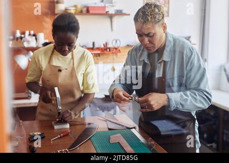 Équipe de deux artisans modernes créant des pièces de cuir faites à la main dans l'atelier Banque D'Images