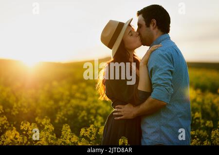 L'amour est tout ce qui compte. Un jeune couple affectueux partage un baiser au coucher du soleil. Banque D'Images