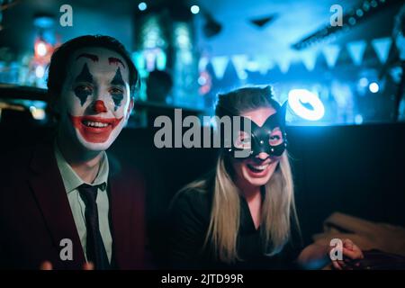 Femme dans le masque de chat et un gars avec le maquillage de joker s'assoit à la table dans le pub. Banque D'Images