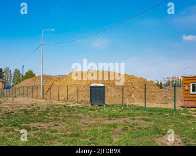 Travaux de terrassement en extérieur avec une grande pile de sable derrière la clôture et une cabine de toilettes extérieures. Banque D'Images