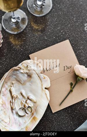 Flatlay de composition de mariage de coquillages de perle avec deux anneaux, invitation, rose blanc frais et flûtes avec champagne sur la table Banque D'Images