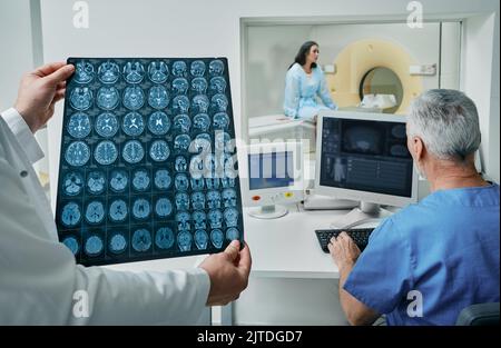 Les radiographes analysant les résultats de l'acquisition CT de la tête du patient se trouvent dans la salle de contrôle du service de radiologie de l'hôpital. TDM ou IRM du cerveau humain Banque D'Images