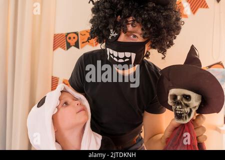 Halloween. Homme et garçon vêtus de squelettes à la fête de la maison, tenant le squelette de jouet Banque D'Images