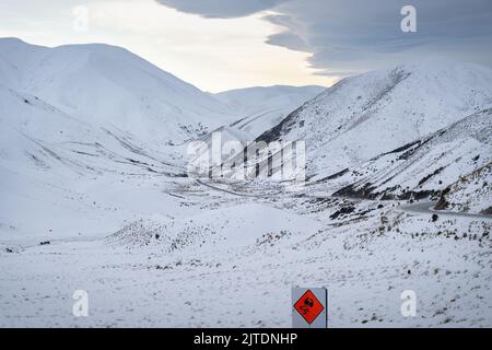 La route longue et sinueuse du col de Lindes est recouverte de neige. Panneau de signalisation de voiture de surface glissante au premier plan, South Island. Banque D'Images