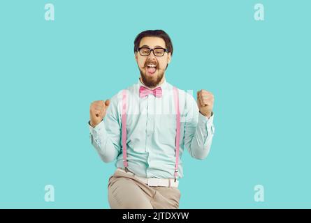Joyeux hipster nerd mâle se réjouit de son succès debout sur fond bleu clair. Banque D'Images