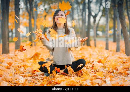 Happy Fall jeune femme souriante joyeuse jette vers le haut feuilles d'automne à l'extérieur dans la forêt d'automne. Race mixte Caucasien, femme d'Asie centrale Banque D'Images