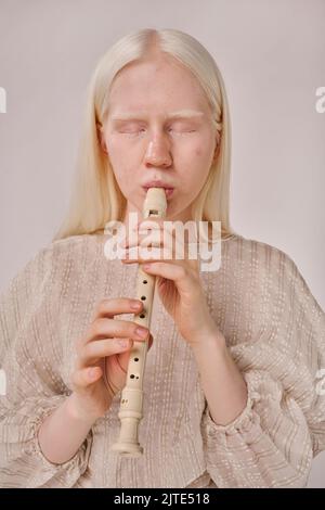 Portrait de la jeune femme albino avec des cheveux blancs appréciant jouer sur la flûte sur fond blanc Banque D'Images